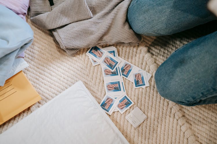 Crop Faceless Person Sitting On Floor With Postage Stamps