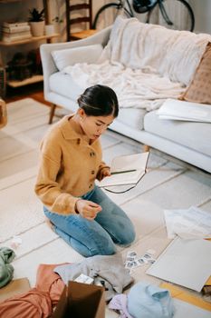 Focused Asian woman preparing parcel and reading notes in notebook