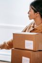Crop concentrated Asian female in warm sweater standing with carton boxes in light post office and looking away thoughtfully