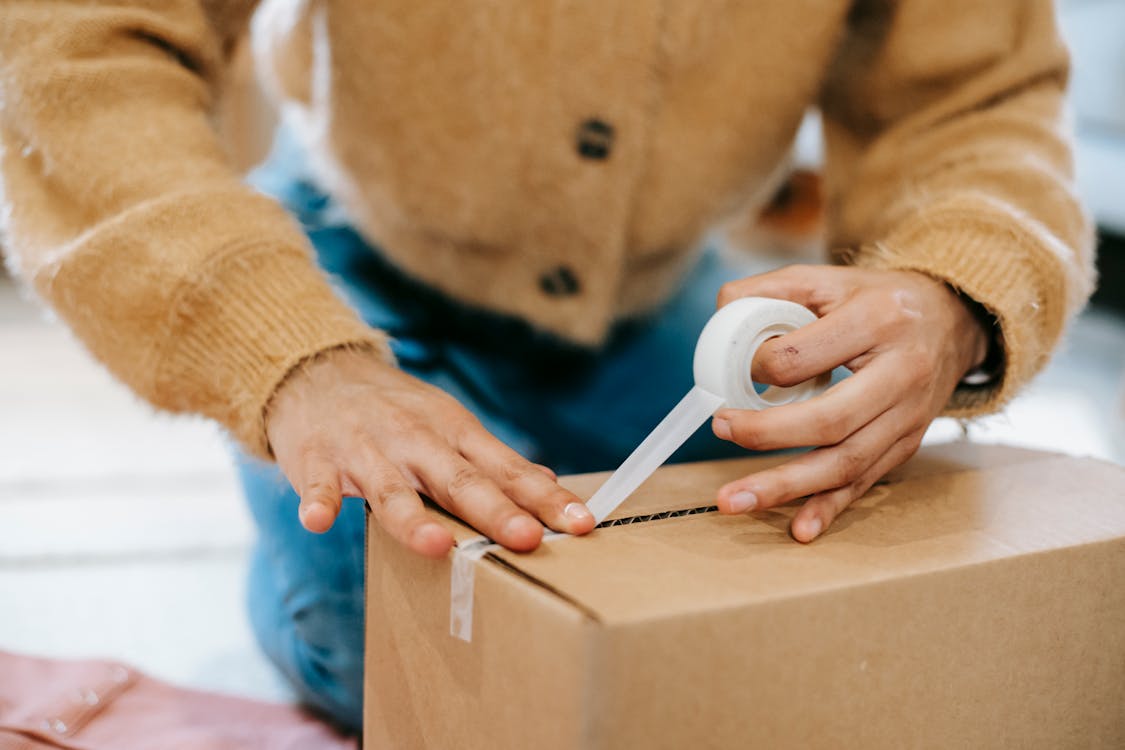 Crop unrecognizable woman sealing carton parcel with tape