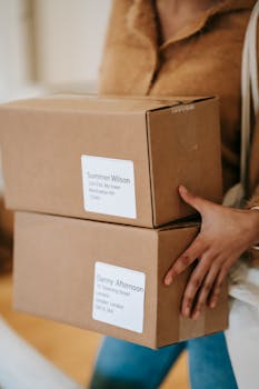 Close-up of a woman holding two labeled cardboard boxes indoors, ready for delivery.