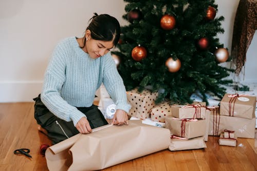 Content Asian woman wrapping present box near Christmas tree