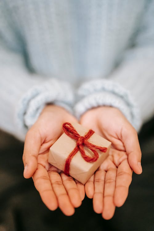 Free High angle crop unrecognizable female in blue sweater demonstrating small wrapped present box on hands Stock Photo