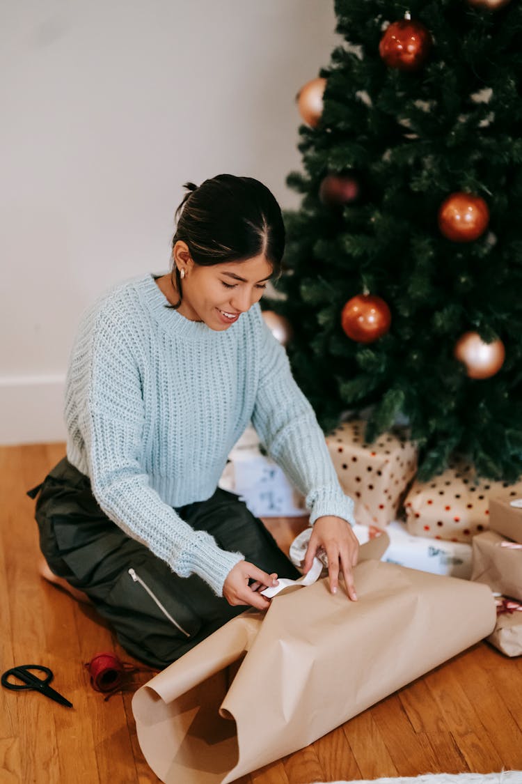 Smiling Asian Woman Wrapping Present Near Christmas Tree