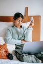 Positive Asian woman making online purchase on bed