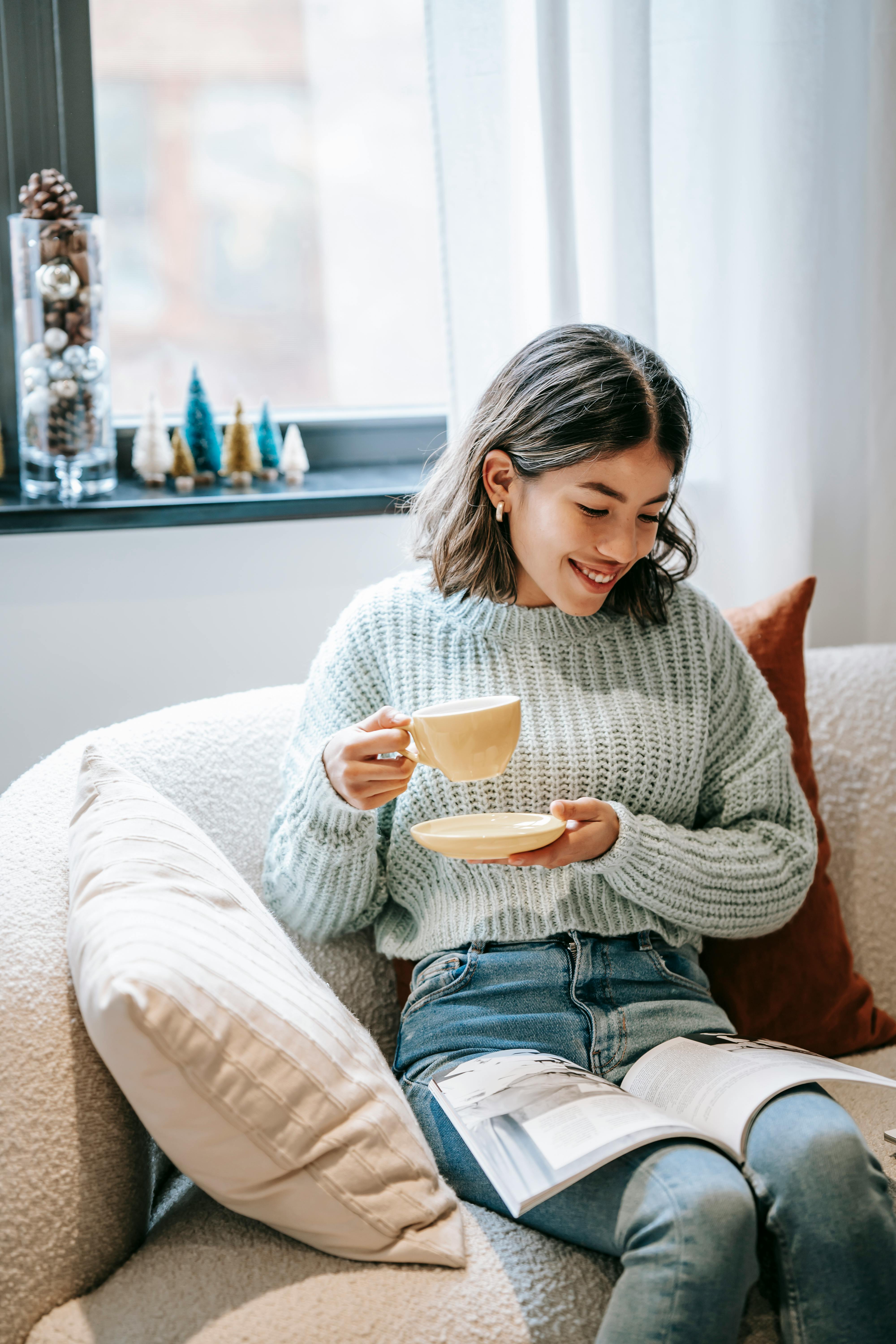 smiling asian woman reading magazine and enjoying hot coffee