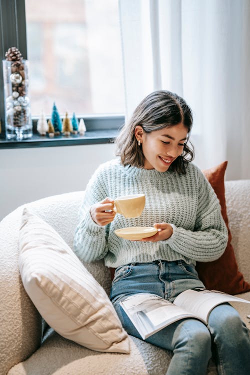 Smiling Asian woman reading magazine and enjoying hot coffee