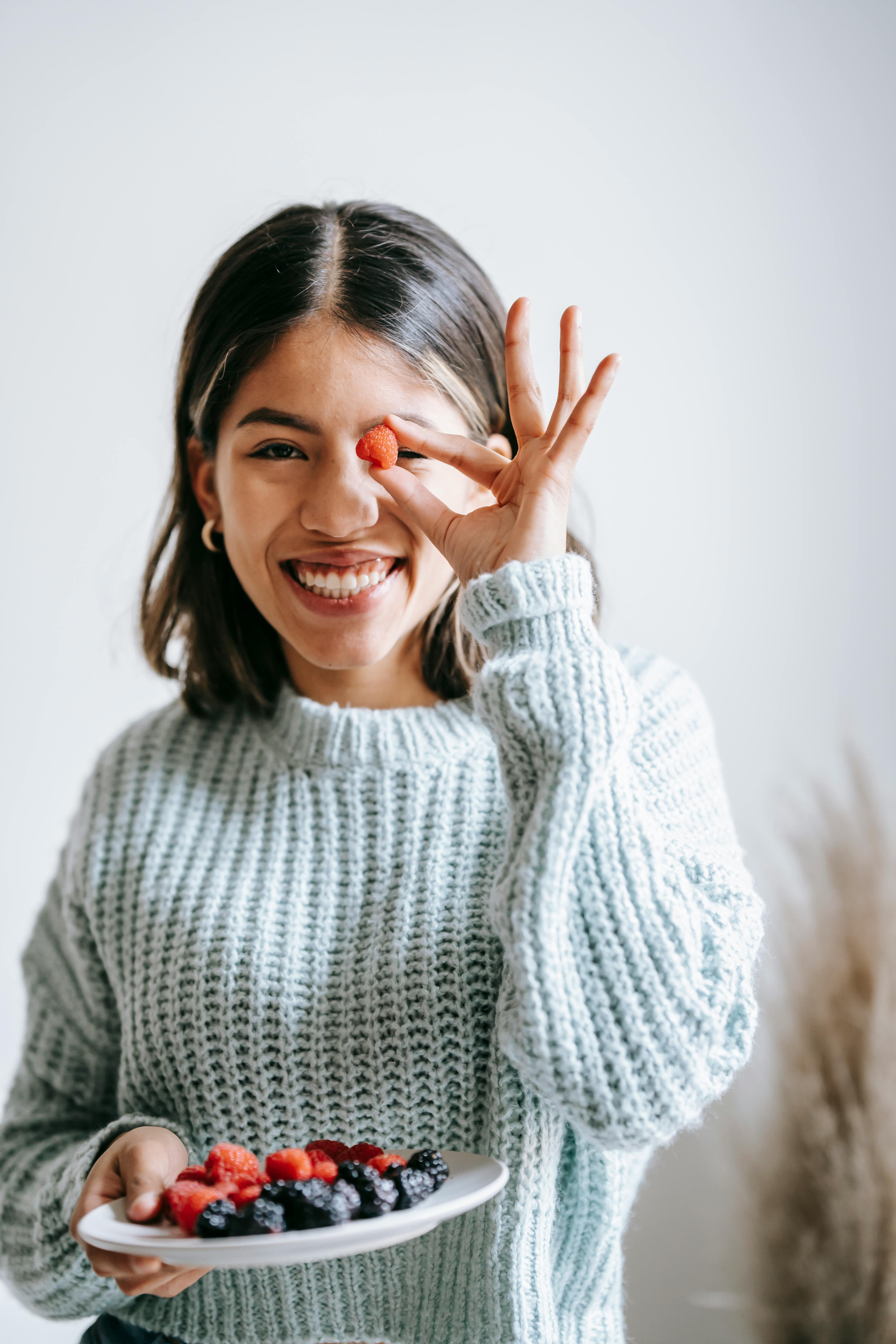 positive young ethnic woman smiling and showing tasty berry