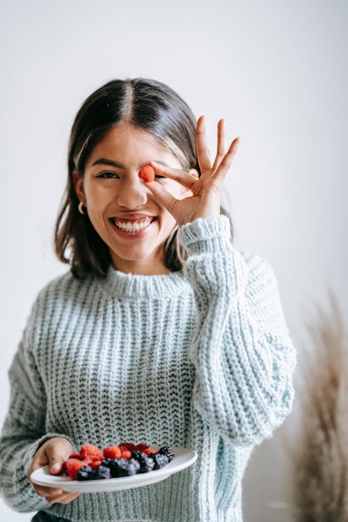 Positive young ethnic woman smiling and showing tasty berry