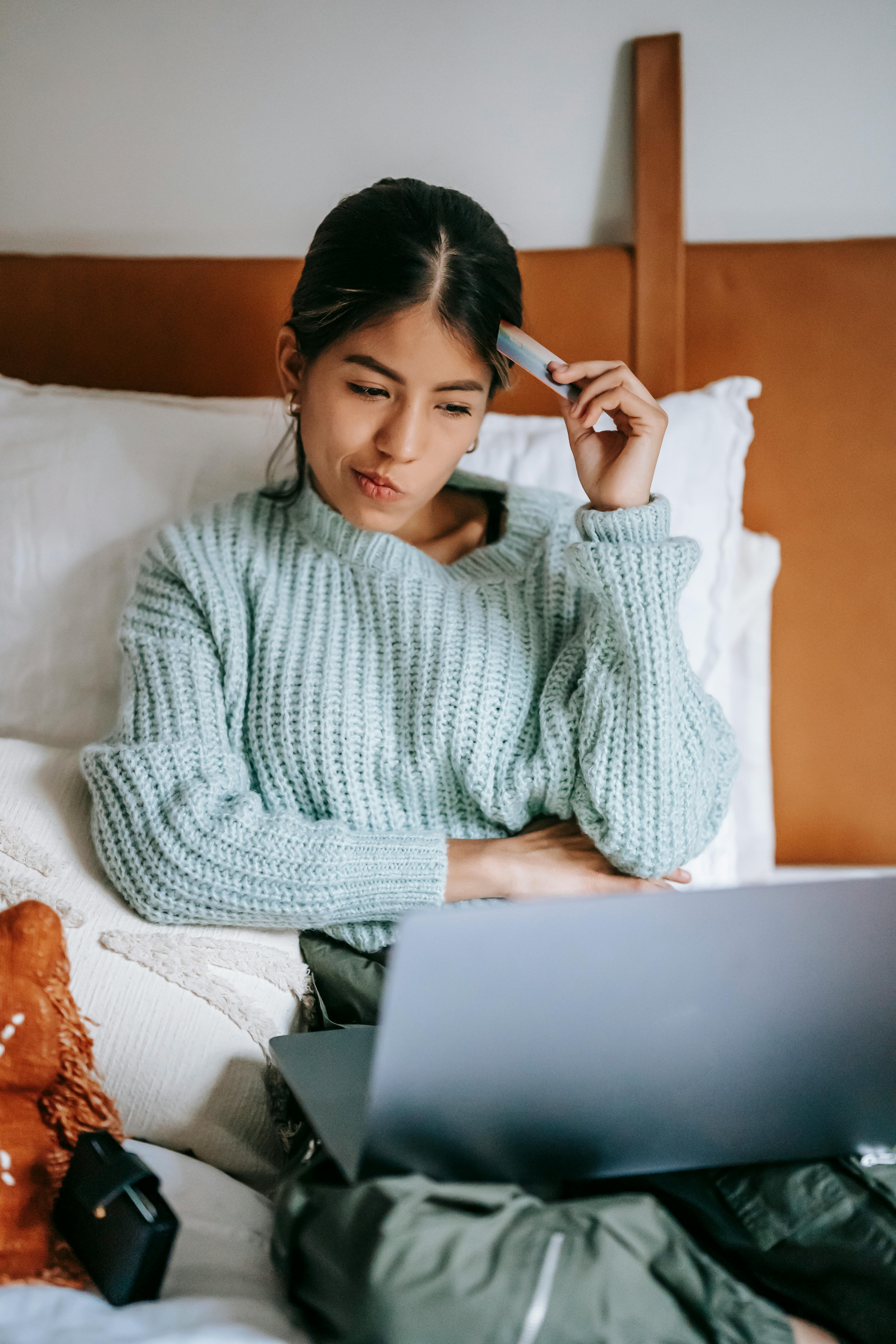 woman with credit card pondering while buying online with laptop