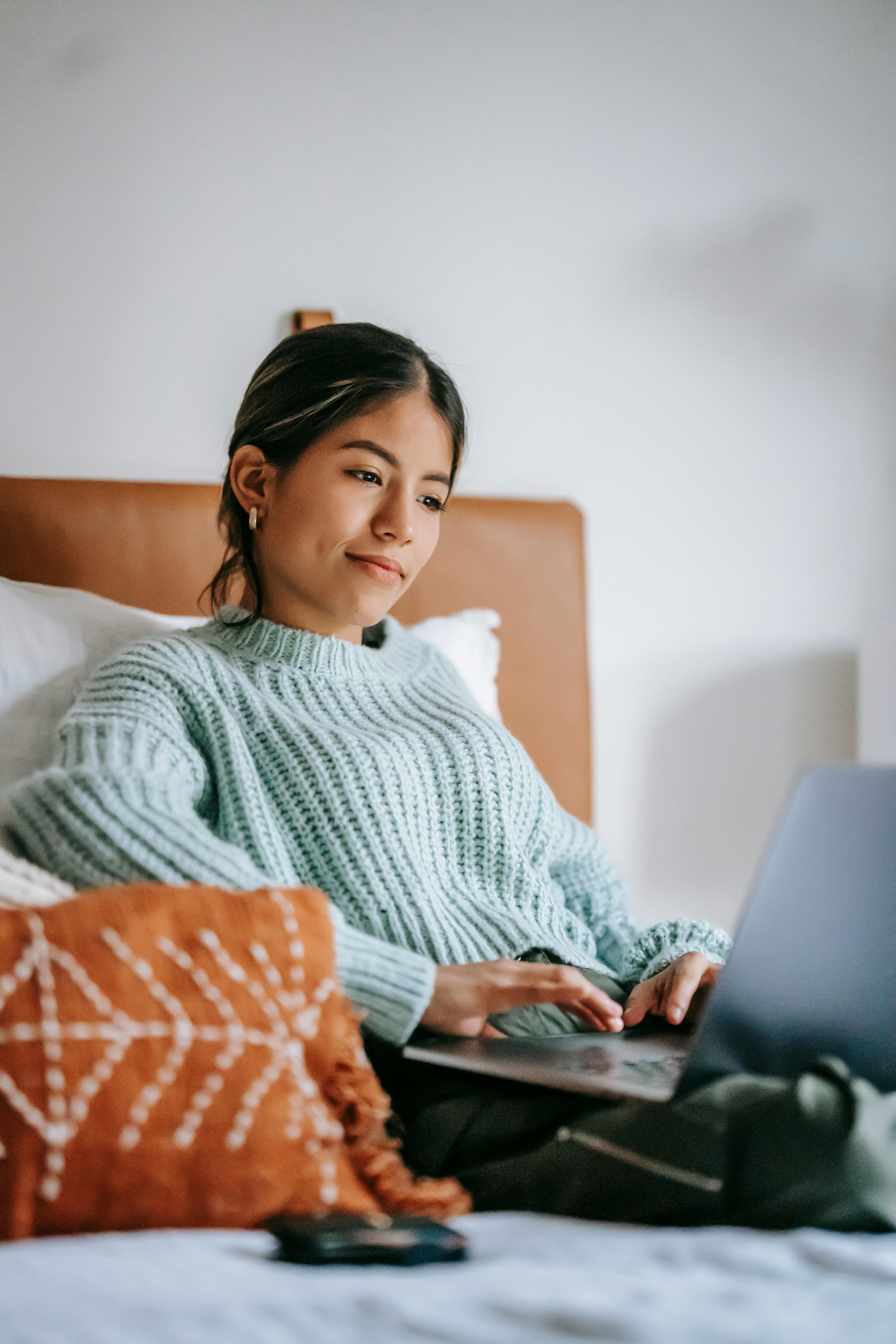 content young ethnic woman freelancing with laptop on bed
