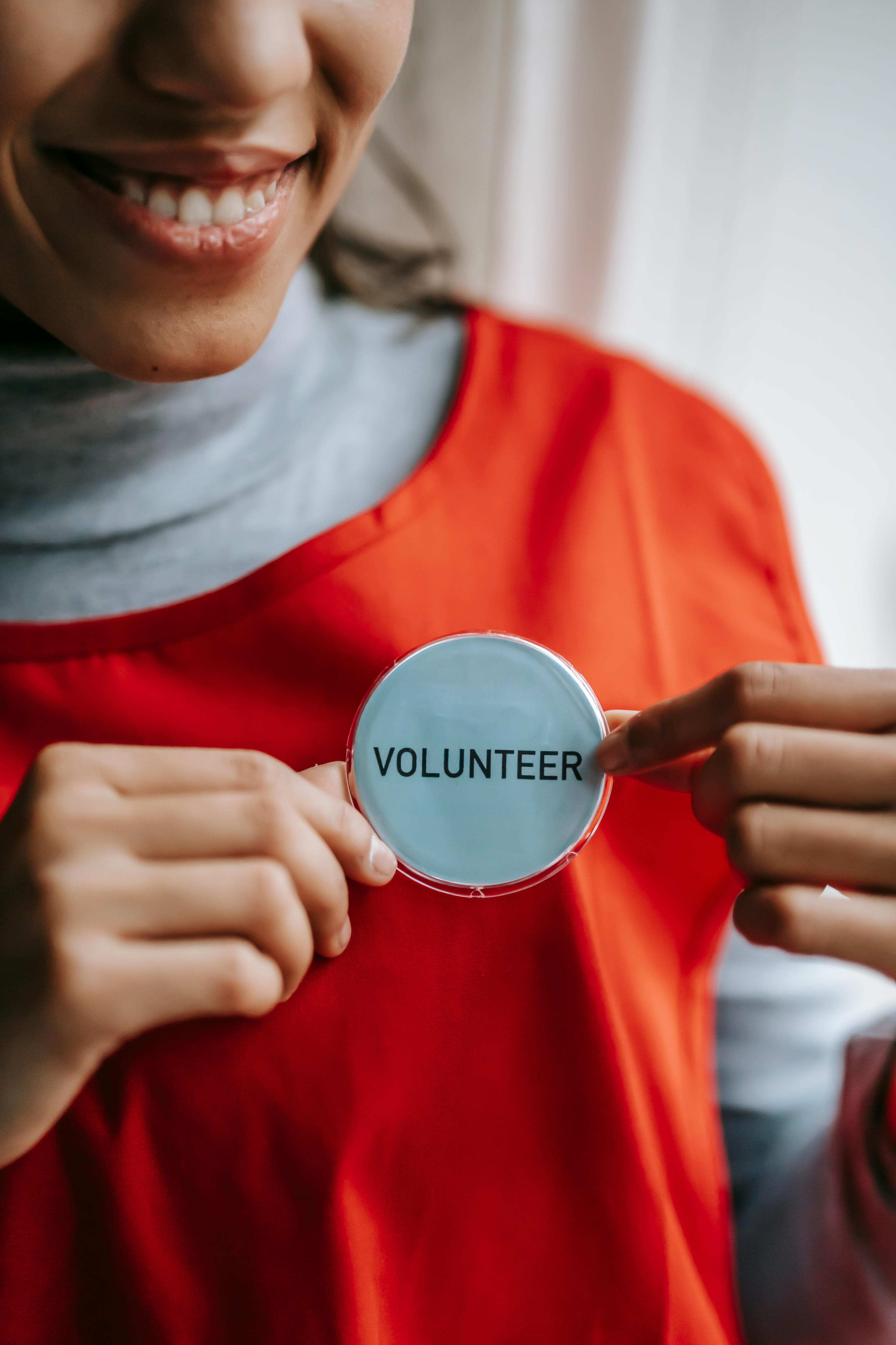 Smiling ethnic woman showing volunteer sign on red apron