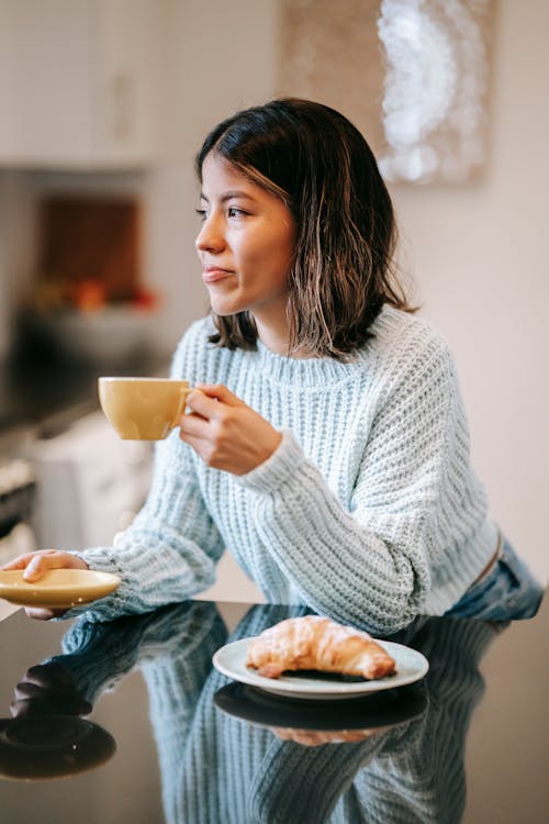 Glad woman drinking coffee at table with croissant