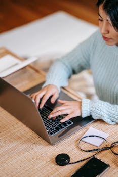 A woman focusing on her laptop, working remotely in a cozy indoor setting.
