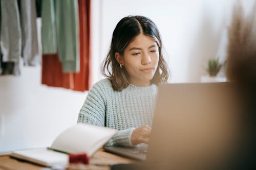Free Young ethnic woman working with laptop at table Stock Photo