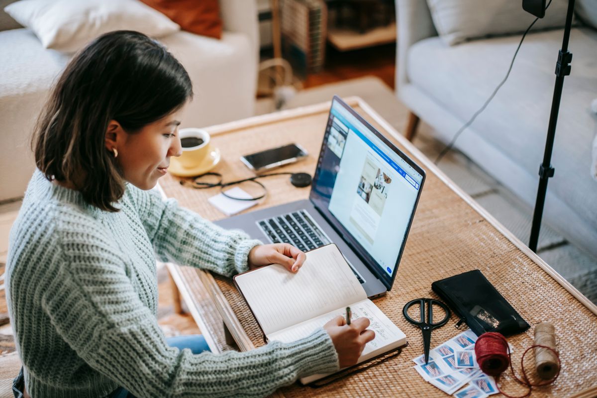 A person comparing notes while working at a laptop