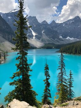 Vibrant turquoise alpine lake surrounded by rugged mountains and tall evergreen trees.
