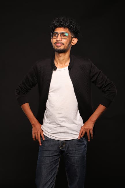 A confident man poses against a dark studio backdrop, exuding style and confidence.