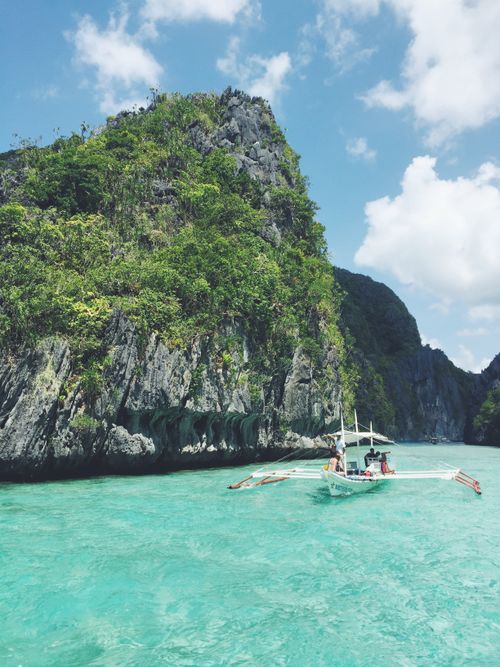 Free A breathtaking view of El Nido, Philippines with a boat sailing past towering cliffs and turquoise waters. Stock Photo