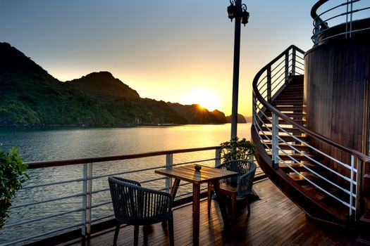 Serene sunset view from a lakeside terrace with chairs and table, capturing summer tranquility.