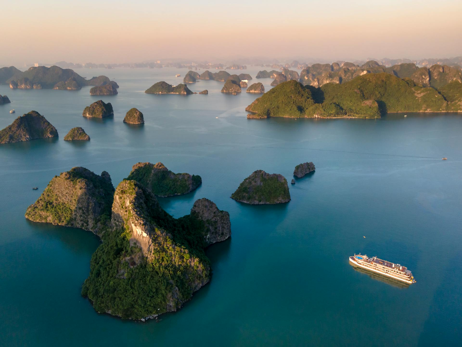 Stunning aerial view of Ha Long Bay's limestone karsts and cruise ship during sunrise.
