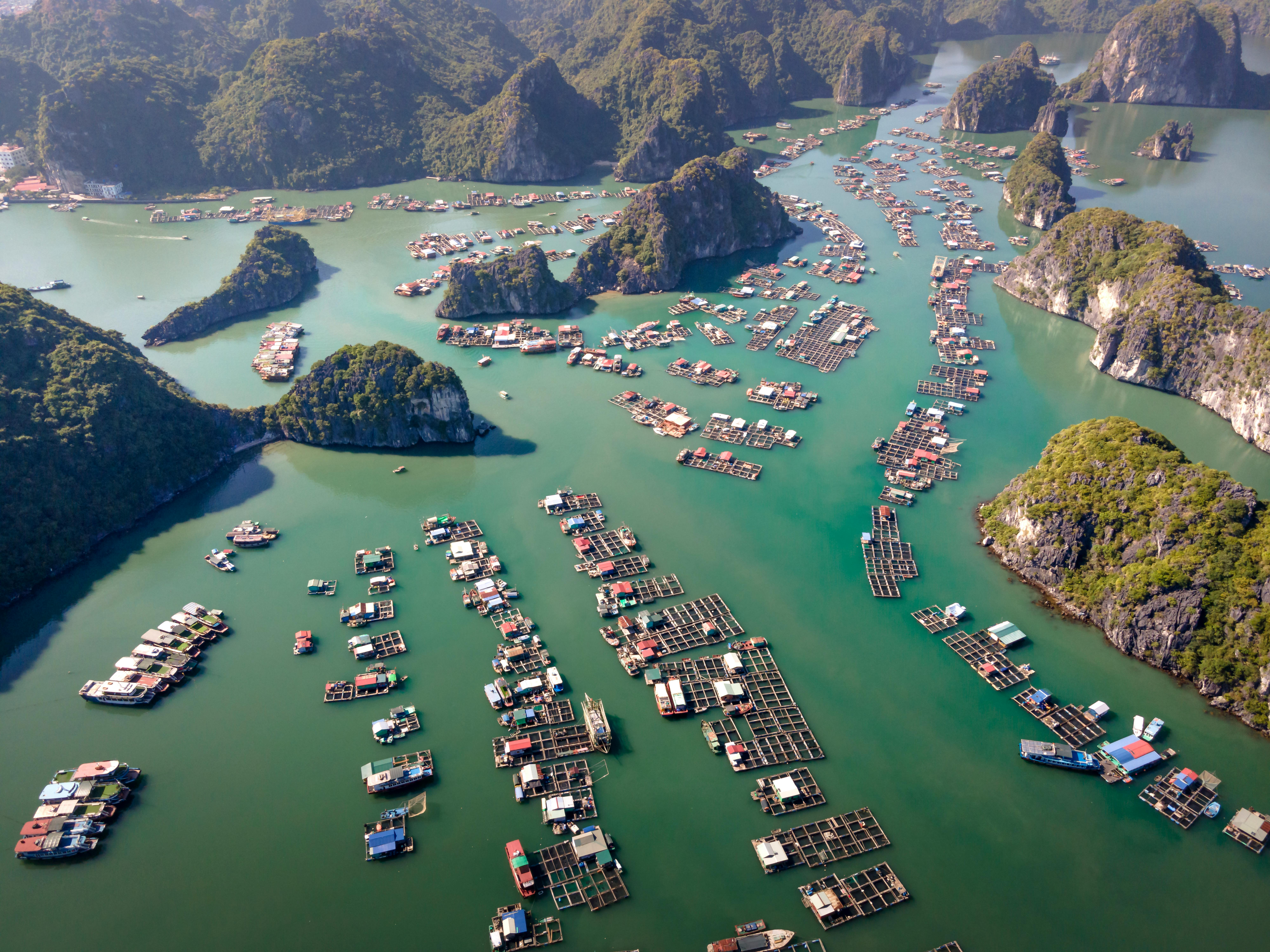 Stunning aerial view of floating villages amidst limestone islands in a serene green bay.