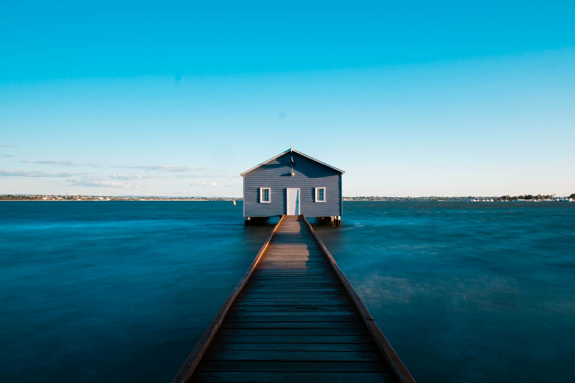 Blue boathouse on ocean with jetty, famous Perth landmark under clear sky.