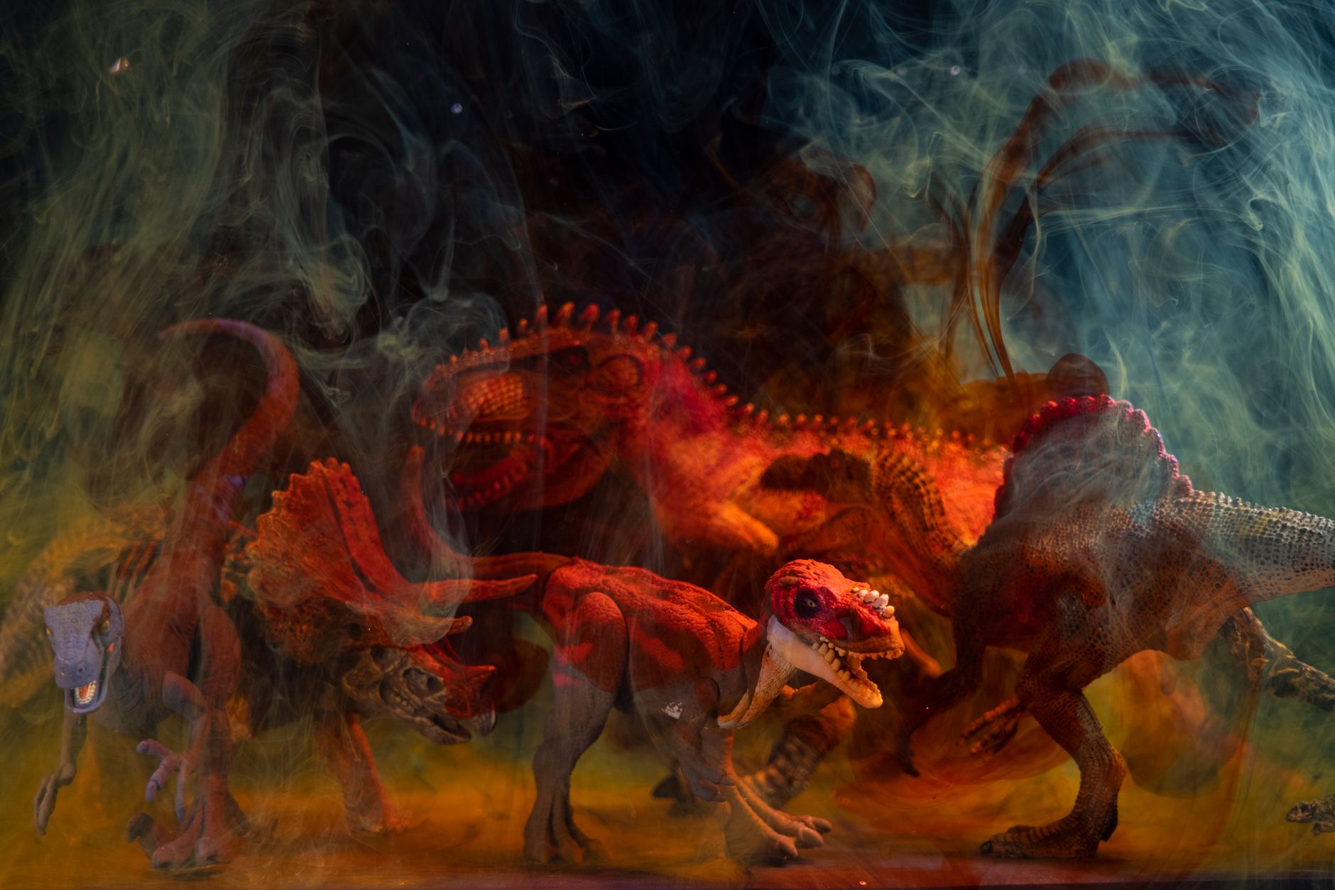 Vibrant dinosaur toy figures enveloped in colored smoke create a dramatic still life composition. — free online jigsaw puzzle on JigsawPuzzlesFreeOnline.org