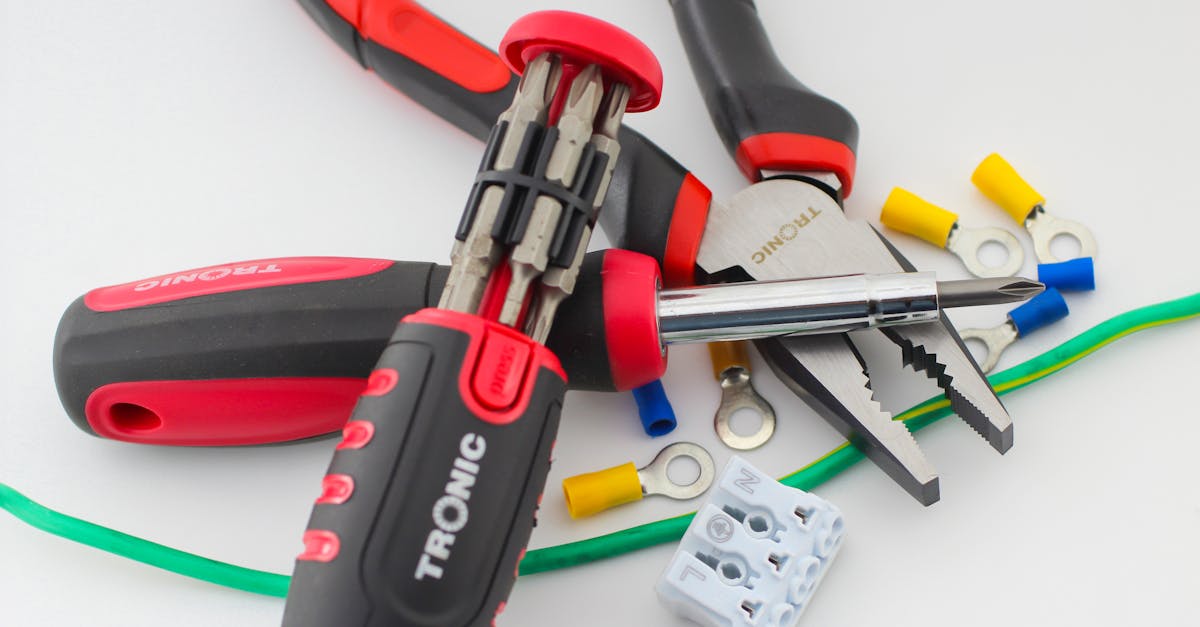 A close-up of essential electrical tools on a white surface, featuring pliers, screwdriver, and colorful cable lugs.