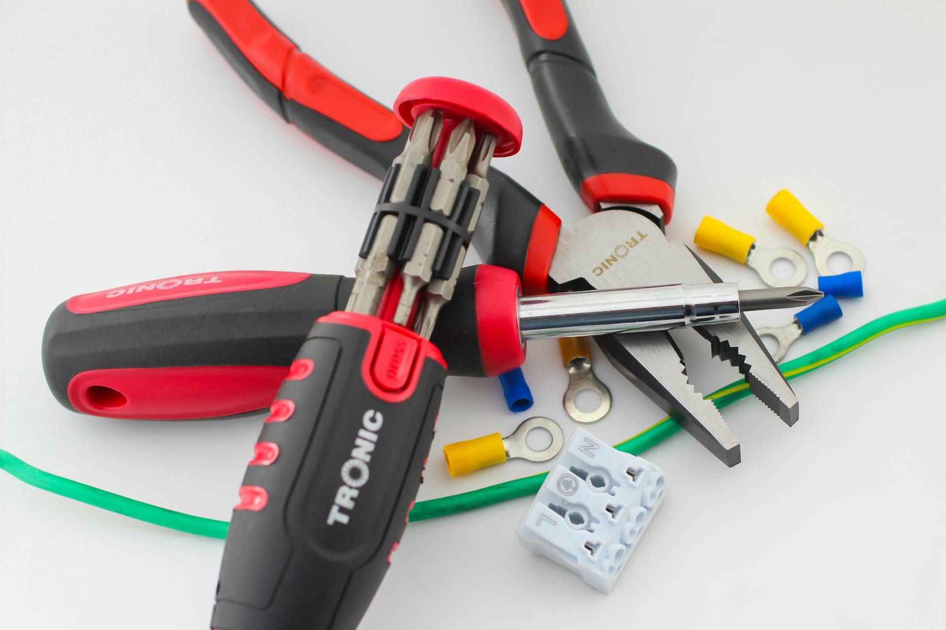 A close-up of essential electrical tools on a white surface, featuring pliers, screwdriver, and colorful cable lugs.