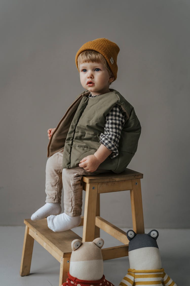 A Boy Wearing A Vest Sitting On A Wooden Ladder