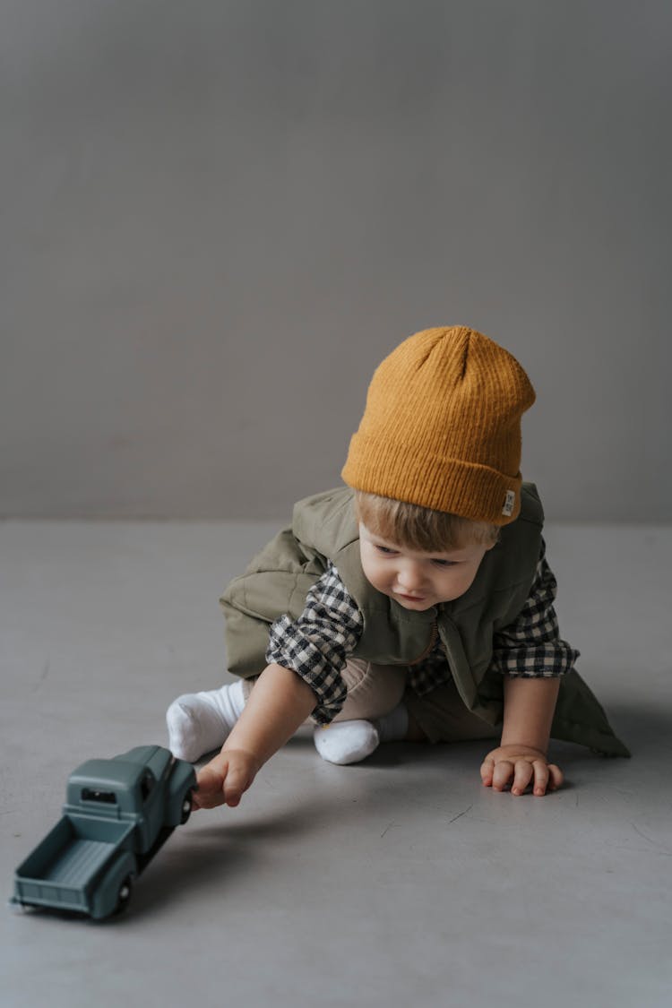 A Baby With A Brown Knit Cap Playing With A Toy Truck