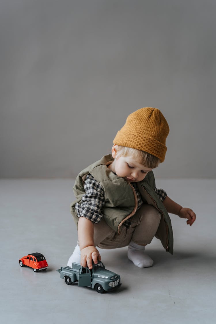 A Toddler With Brown Knit Cap Playing With A Toy Truck