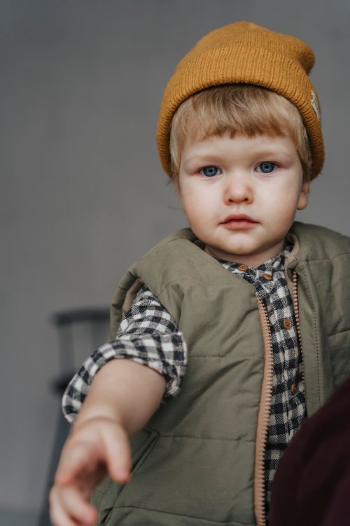 Free A cute child in a knit cap and vest, reaching out with curiosity indoors. Stock Photo