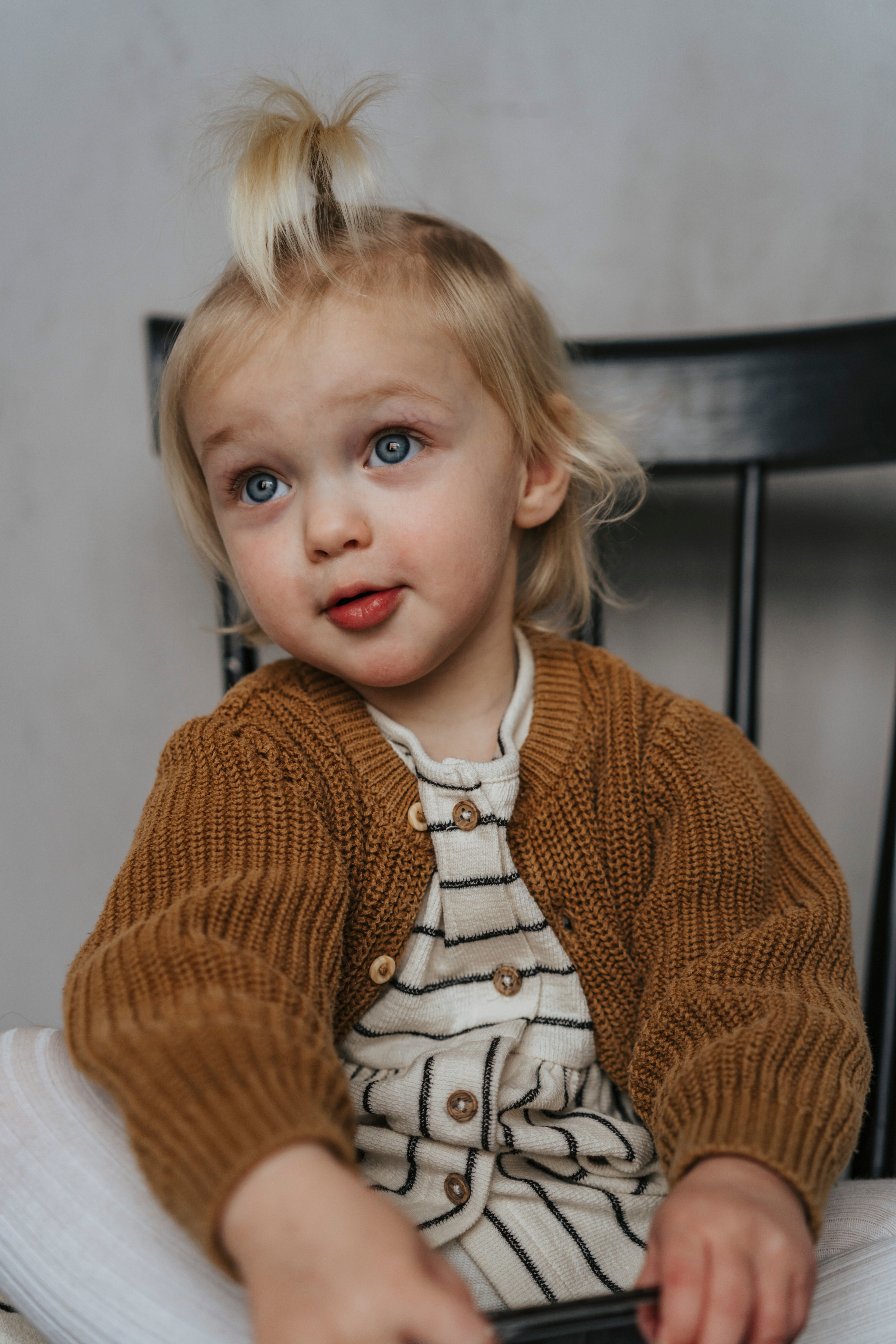 Cute portrait of a young child in a striped dress and sweater, looking up with innocence.