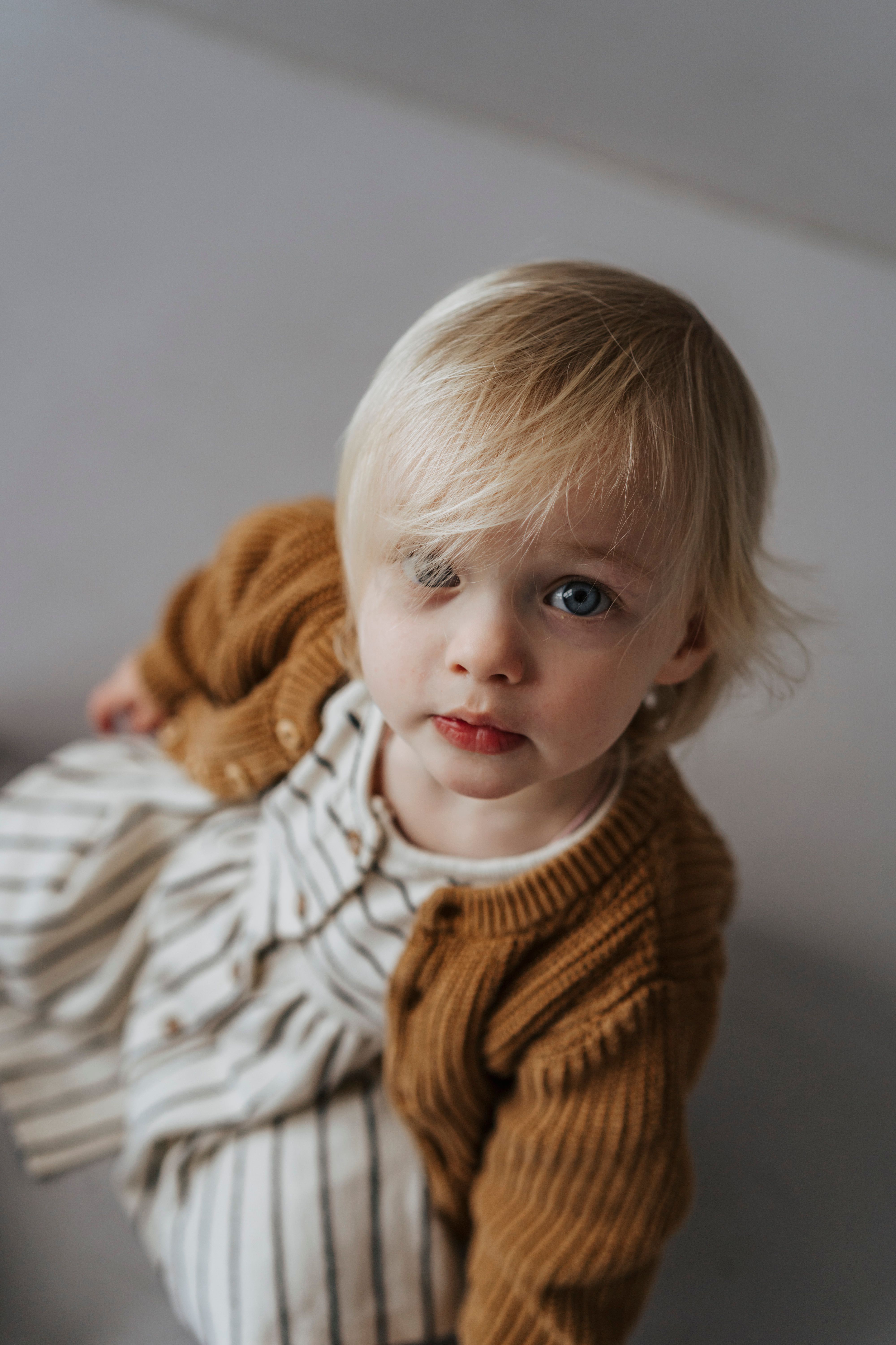 Charming portrait of a blonde toddler in a striped dress and sweater looking up.