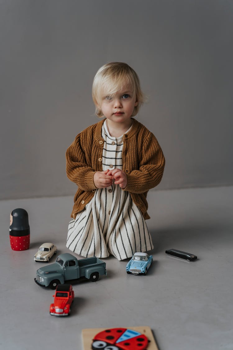 A Pretty Toddler Sitting On Floor With Toy Cars