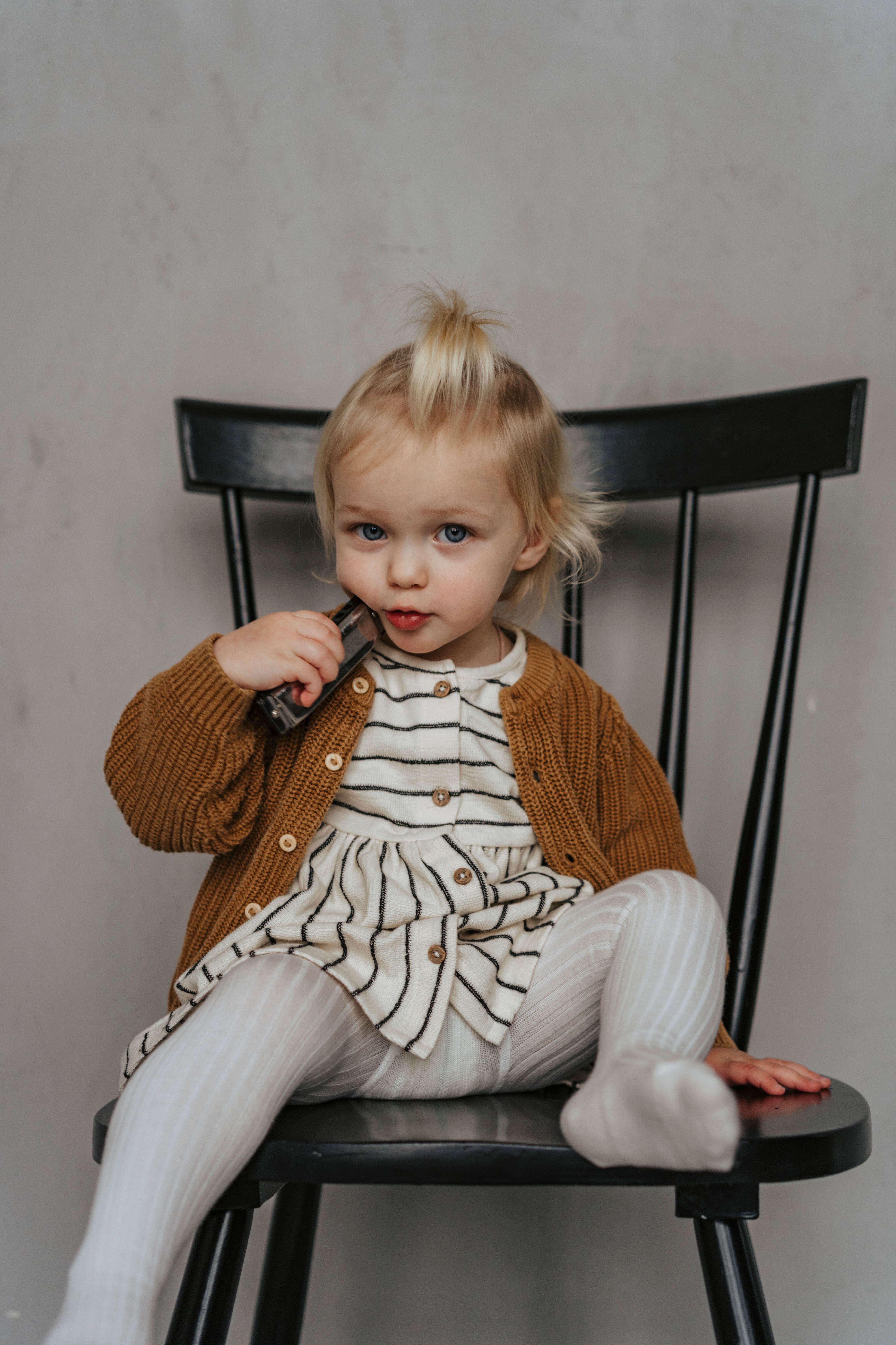 Charming portrait of a toddler girl sitting on a black chair indoors, adding a cute and candid mood.