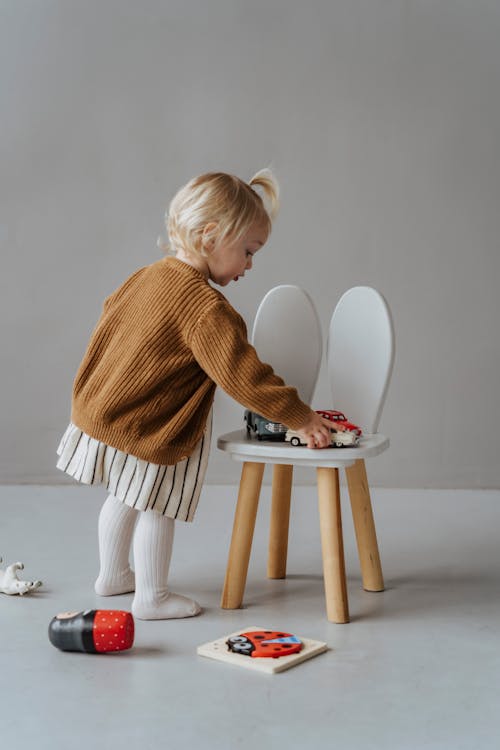 Girl in Brown Sweater Standing beside Brown and White Wooden Chair
