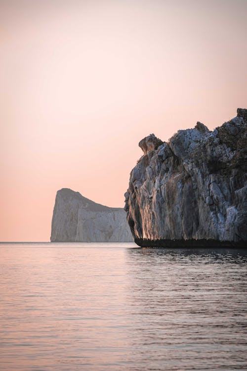 Scenic landscape of cloudless pink sunset sky over rippling ocean with huge rocky cliffs