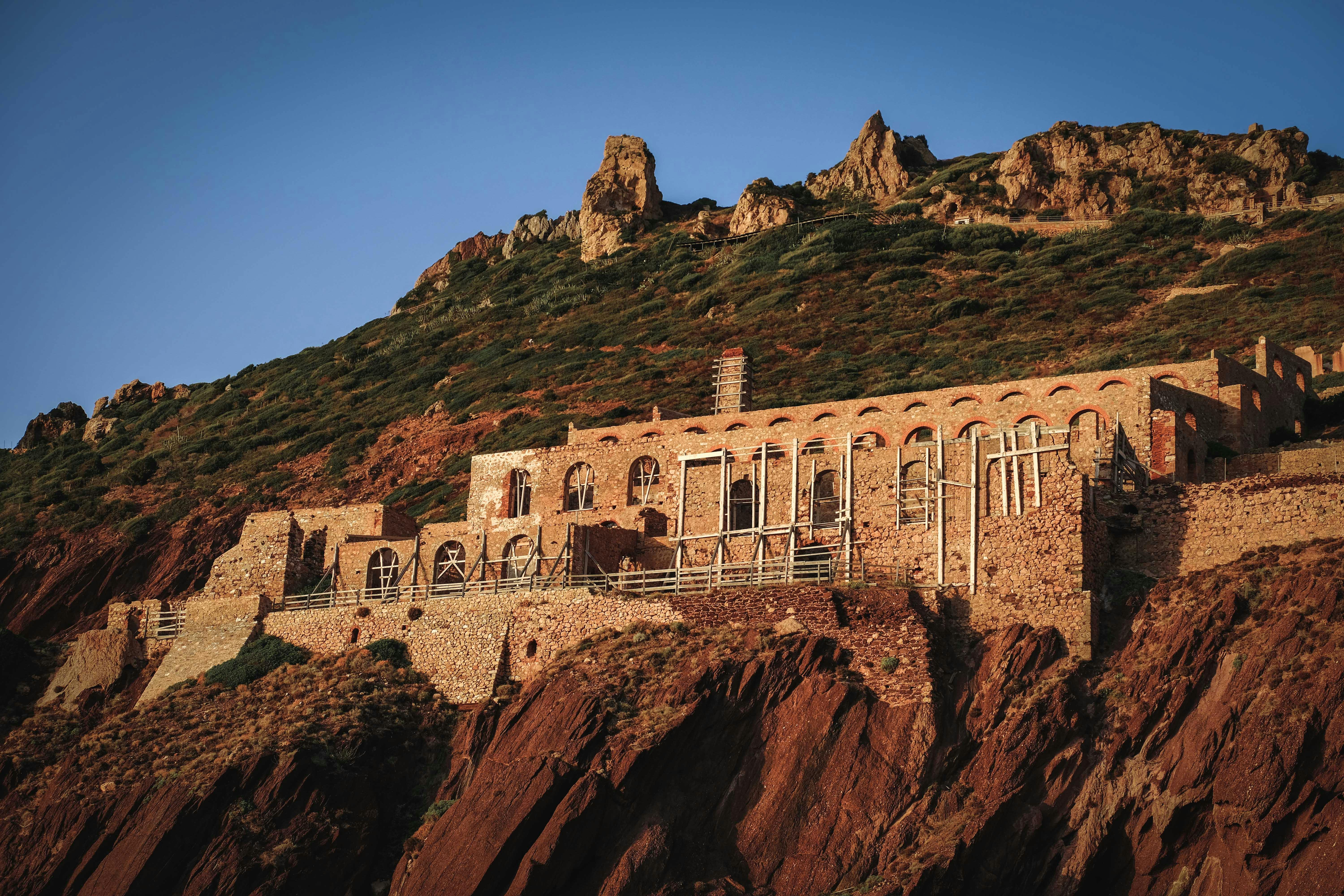 Ruins of old mining complex on rough rocky cliff against blue sky