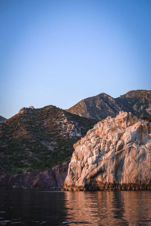 Rocky coast of calm sea against blue sky · Free Stock Photo