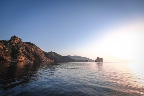 Free Bright sun shining in blue sky over sea surrounded by rocky hills and reflecting in rippling water Stock Photo