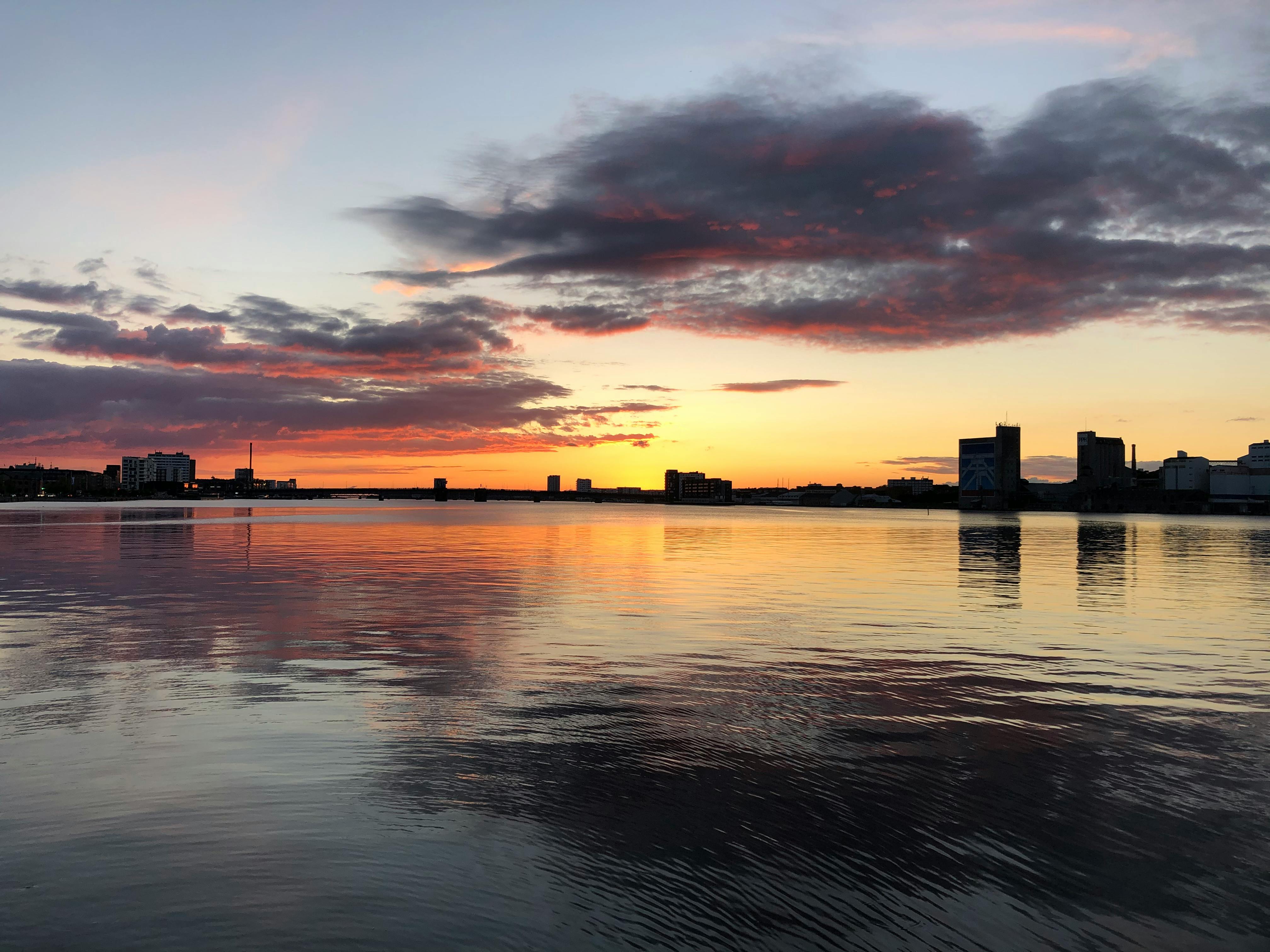 Captivating sunset with city skyline reflection on water in Aalborg, Denmark.