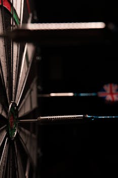 A close-up image of darts hitting the bullseye on a dartboard against a black background.