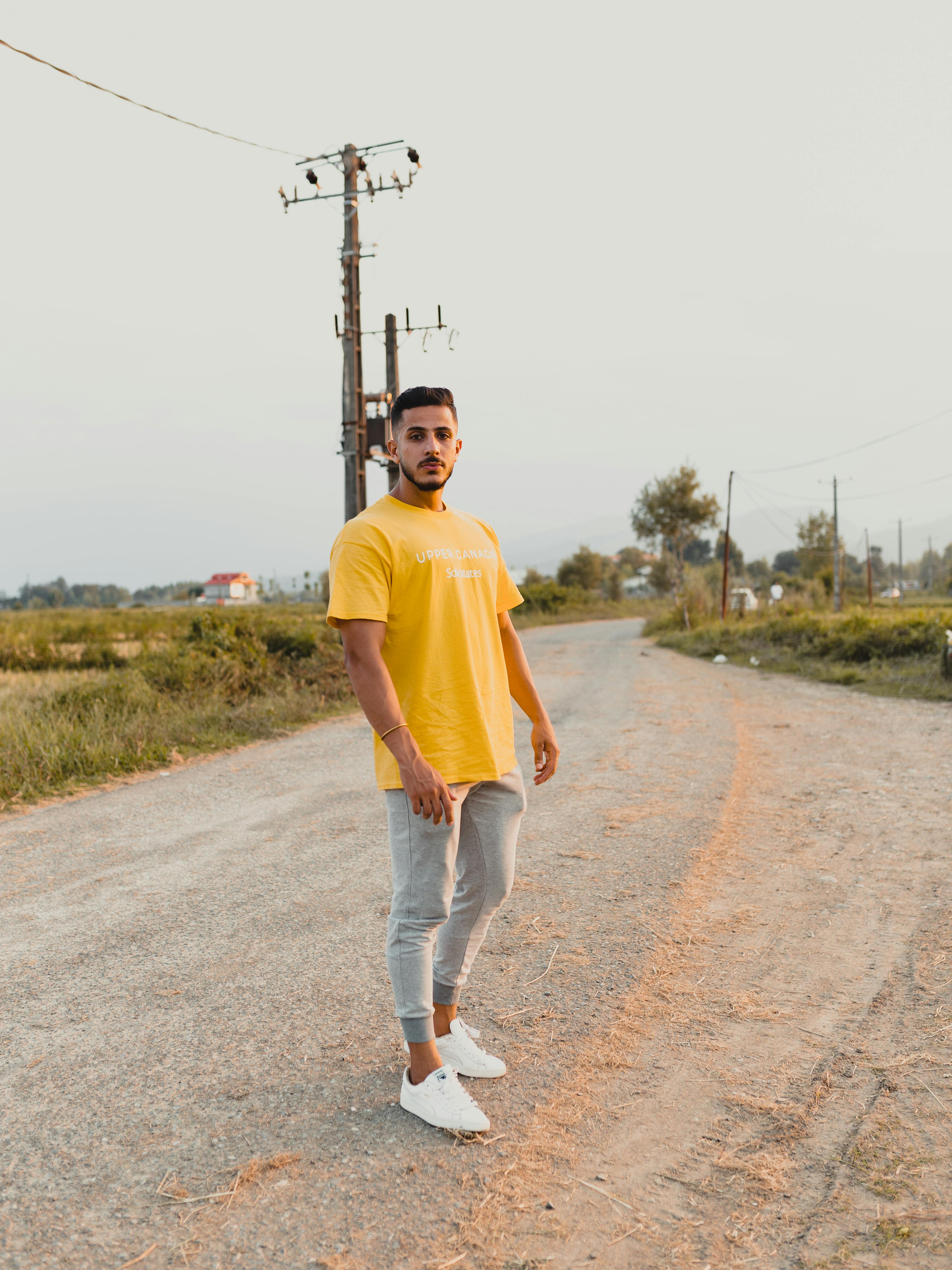man in yellow shirt and gray pants standing on concrete road