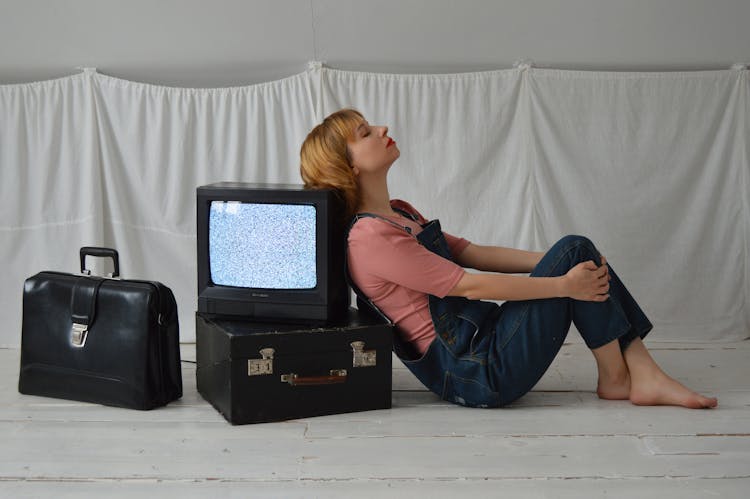 Thoughtful Woman Laying Back On Retro TV Set On Floor