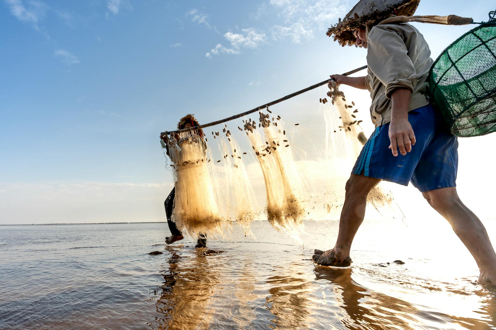 Two fishermen wade through shallow waters hauling nets at sunrise, capturing morning sea bounty.