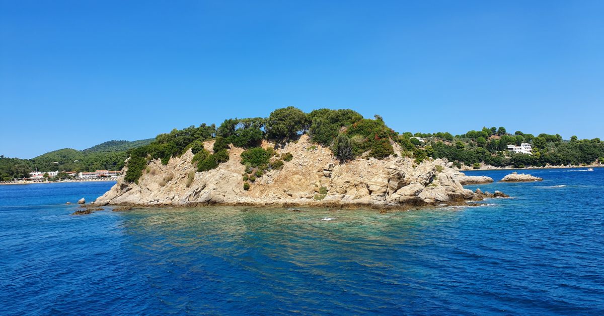 Explore the tranquil beauty of a small island in the Sporades, Greece, surrounded by clear blue sea.