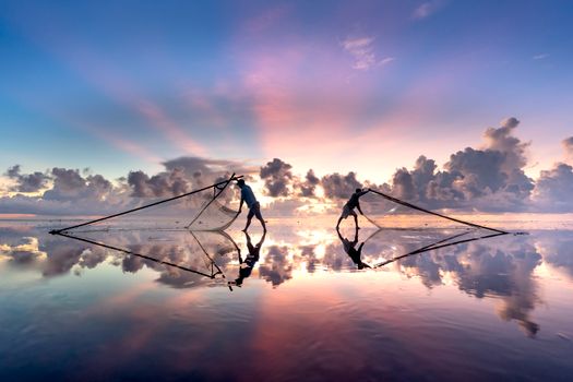 Silhouetted fishermen casting nets during a vivid sunset over tranquil waters.